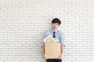 An Asian man stands sad in an office after being fired, keeping personal belongings in cardboard boxes. photo