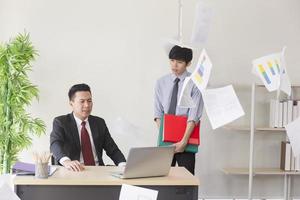 An angry Asian manager, his employees unable to work as expected, throwing paper in the office. photo