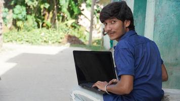 A poor boy with laptop attending class in village online class photo