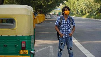 a boy at bus stand wearing mask in road behind auto photo