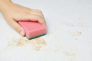 Cleaning kitchen table. Pink sponge in woman hand removes dirt, bread crumbs and leftovers. Household chores photo