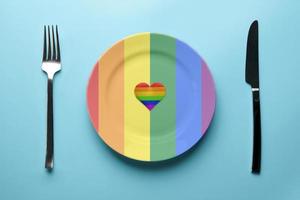 Plate in LGBT flag colors. Pride flag concept. Romantic LGBT festival feast. Date with lonely lesbian, gay, bisexual or transgender in cafe. photo