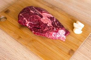 carne de res en tabla de cortar de madera en la cocina. vista superior del bistec crudo crudo con ajo. cerrar deliciosa cocina moderna.