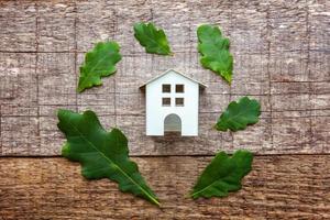 Toy House and green oak leaves on wooden background photo