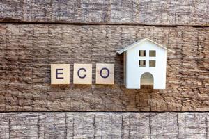 Miniature toy model house with inscription ECO letters word on wooden background photo