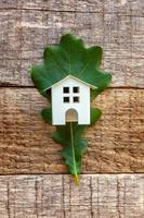 Toy House and green oak leaf on wooden background photo