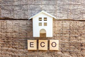 Miniature toy model house with inscription ECO letters word on wooden background photo