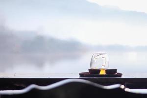 Morning cup of hot tea with lake background at sunrise. photo