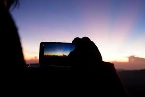 A wonderful scenery of a sunrise on the top of the mountain, a tourist is taking a picture of the sunrise with his phone photo