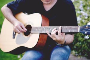 Picture of a guitarist, a young man playing a guitar while sitting in a natural garden,music concept photo