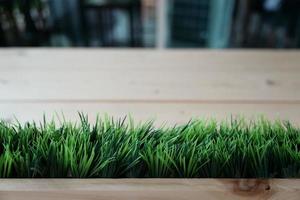 artificial green grass arranged in the horizontal row at the front of plank wooden table blur background. photo