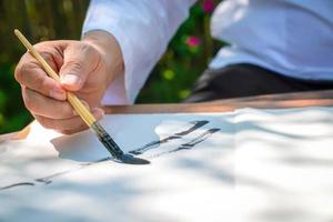 Senior man drawing bamboo tree by Asia China brush with Asian stroke style. He's sitting in the relaxing bambook garden. photo