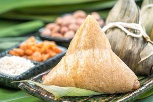 primer plano, espacio de copia, famosa comida china en el festival dragon boat duan wu, albóndigas de arroz al vapor en forma piramidal envueltas en hojas de bambú hechas con ingredientes crudos de arroz pegajoso foto