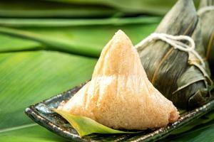 primer plano, espacio de copia, famosa comida china en el festival dragon boat duan wu, albóndigas de arroz al vapor en forma piramidal envueltas en hojas de bambú hechas con ingredientes crudos de arroz pegajoso foto