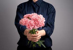 Young girl in dark blue striped shirt giving bunch of handmade beautiful blooming baby pink color carnations as a gift for mothers day concept, close up, copy space, clipping path photo