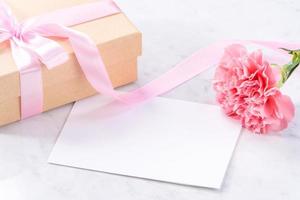 May mothers day handmade giftbox idea concept, beautiful blooming carnations with baby pink ribbon bow gift isolated on modern marble desk, close up, copy space, mock up photo