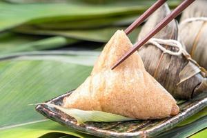 primer plano, espacio de copia, famosa comida china sabrosa en el festival dragon boat duan wu, albóndigas de arroz al vapor en forma piramidal envueltas en hojas de bambú hechas con ingredientes crudos de arroz pegajoso foto