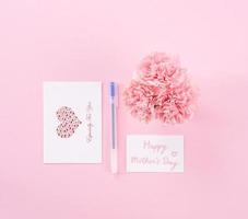 Top view, flat lay, mock up, copy space, handwritten greeting card template isolated with pale pink background, idea concept of thanks, wishes, craft carnations bouquet photo