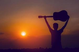 The silhouette of a guitarist who holds a guitar and has a sunset, silhouette concept. photo