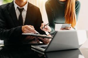 Business documents on office table with smart phone and laptop and two colleagues discussing data in the background photo