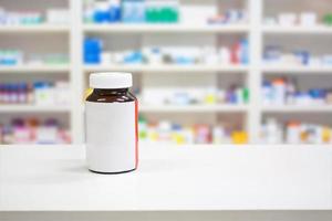 Blank white label medicine bottle on counter with blur shelves of drug in the pharmacy drugstore photo