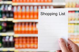 Sostenga a mano el papel de la lista de compras sobre las botellas de refrescos en los estantes foto