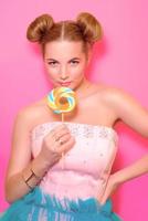 Portrait of stylish cute young blonde woman with colorful lollipop on pink background photo