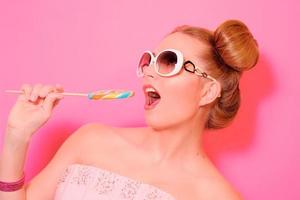 Portrait of stylish cute young blonde woman with colorful lollipop on pink background photo