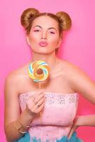 retrato de una joven rubia elegante y linda con una piruleta de colores en el fondo rosa foto