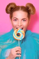 Portrait of stylish cute young blonde woman with colorful lollipop on pink background photo