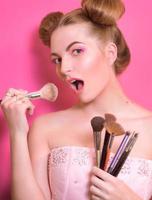 attractive blonde woman with colorful make up with cosmetic brushes and shadows in her and make up master's hands photo
