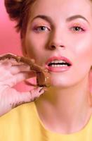 portrait of cute attractive blonde young woman with chocolate candy in her fingers