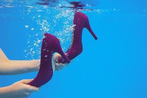 Violet velvet shoes in woman hands underwater in the swimming pool on blue background photo