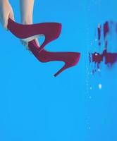 Violet velvet shoes in woman hands underwater in the swimming pool on blue background photo