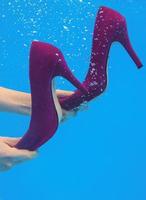 Violet velvet shoes in woman hands underwater in the swimming pool on blue background photo