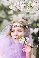 beautiful young blonde woman in flower wreath blooming trees in spring photo