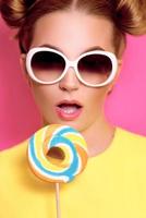 Portrait of stylish cute young blonde woman with colorful lollipop on pink background photo