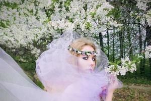 beautiful young blonde woman in flower wreath blooming trees in spring photo