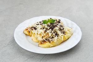 Pisang panggang, Grilled banana topped with chocolate sprinkles, grated cheese, and sweet white milk. Served on plate with mint leaves on grey background. photo