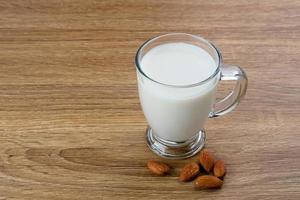 Almond milk in glass with almonds on wooden table. Space for text photo