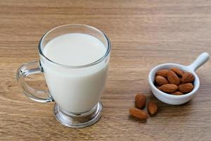 Almond milk in glass with almonds on wooden table. Space for text photo