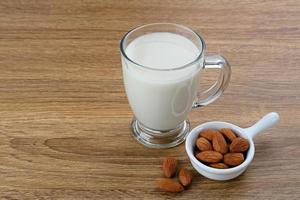 Almond milk in glass with almonds on wooden table. Space for text photo
