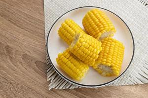 Jagung manis rebus or boiled sweet corn slices served on bowl on wooden background. Space for text. photo