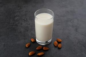 Almond milk in glass with almonds on wooden table. Space for text photo