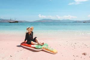 Blonde woman in summer hat and sunglasses relaxing on inflatable mattress in pink sandy beach photo