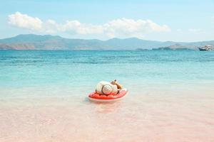 A girl with summer hat laying on inflatable water mattress in pink sandy beach enjoying summer holiday photo