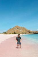 Asian man in sunglasses running on pink sand beach at Labuan Bajo photo