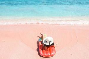 Woman in summer hat relaxing on inflatable in pink sandy beach at Labuan Bajo photo