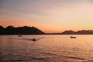 Black silhouette of hills with traditional boat sailing on the sea at Labuan Bajo photo