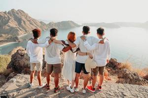 grupo de amigos con camisa blanca y vestido abrazándose unos a otros en la cima de la colina mientras miran el paisaje foto